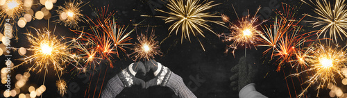 Happy New Year   Silvester   Party background banner panorama greeting card - Young happy people holding sparkling sparklers in her hands at dark night  with golden bokeh lights and firework
