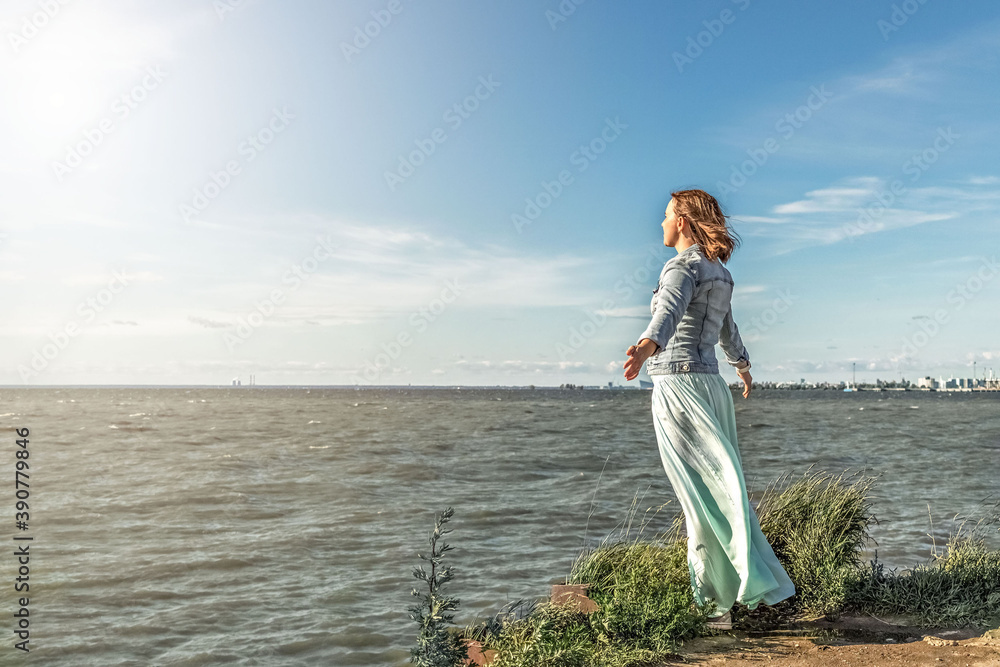 Young woman stands in the wind at the edge of the seashore