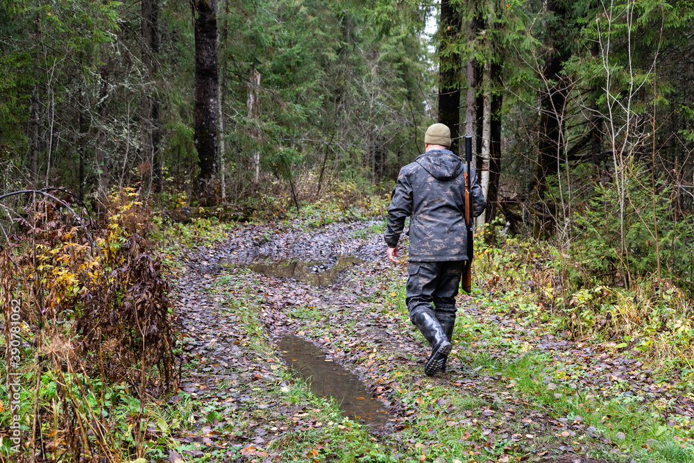 Hunter with a gun walks along a forest road	