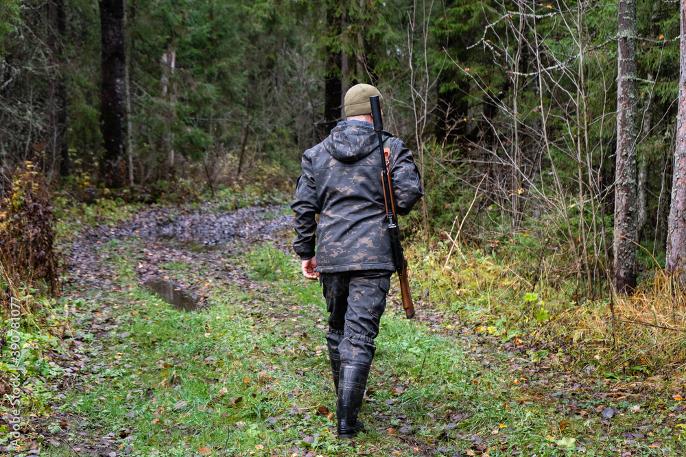 Hunter with a gun walks along a forest road	