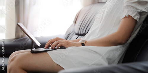 Cropped shot of woman hands typing on computer laptop while sitting on couch in living room.