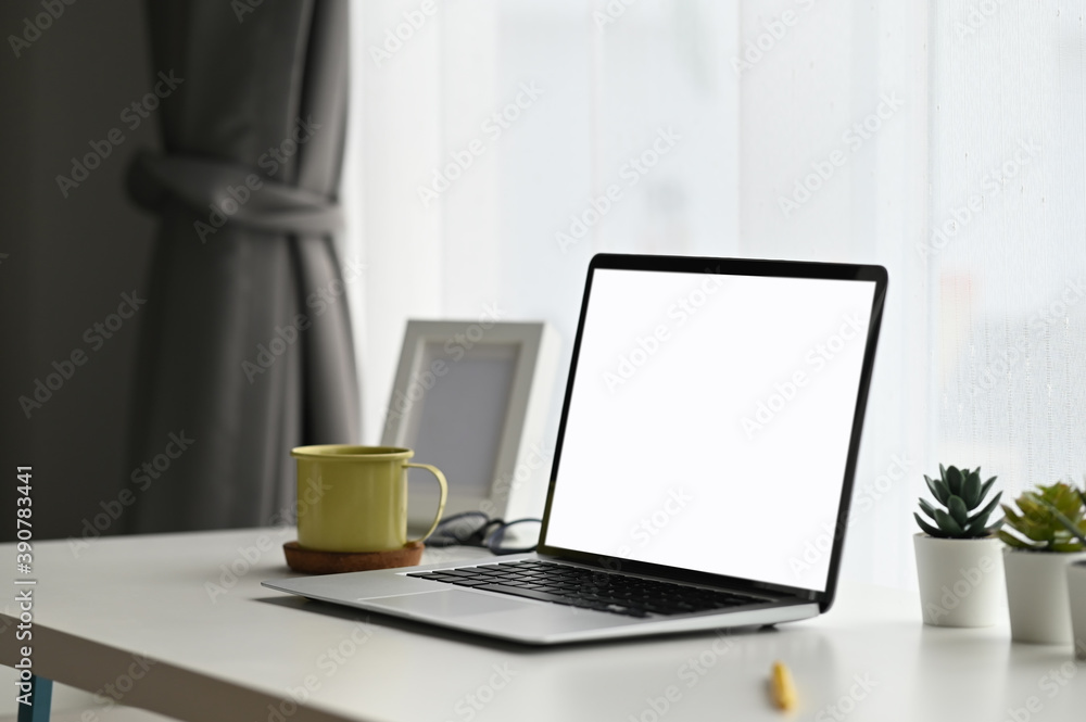 Contemporary workspace with with screen laptop computer, plant and coffee cup on white table.