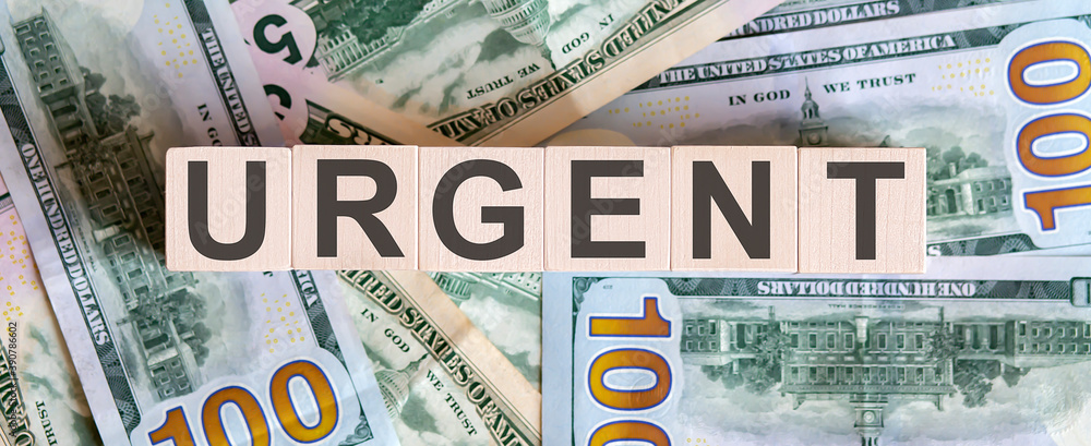 Concept words URGENT on wooden blocks on a beautiful background from dollar bills. Concept words URGENT on wooden blocks on a beautiful background from dollar bills.