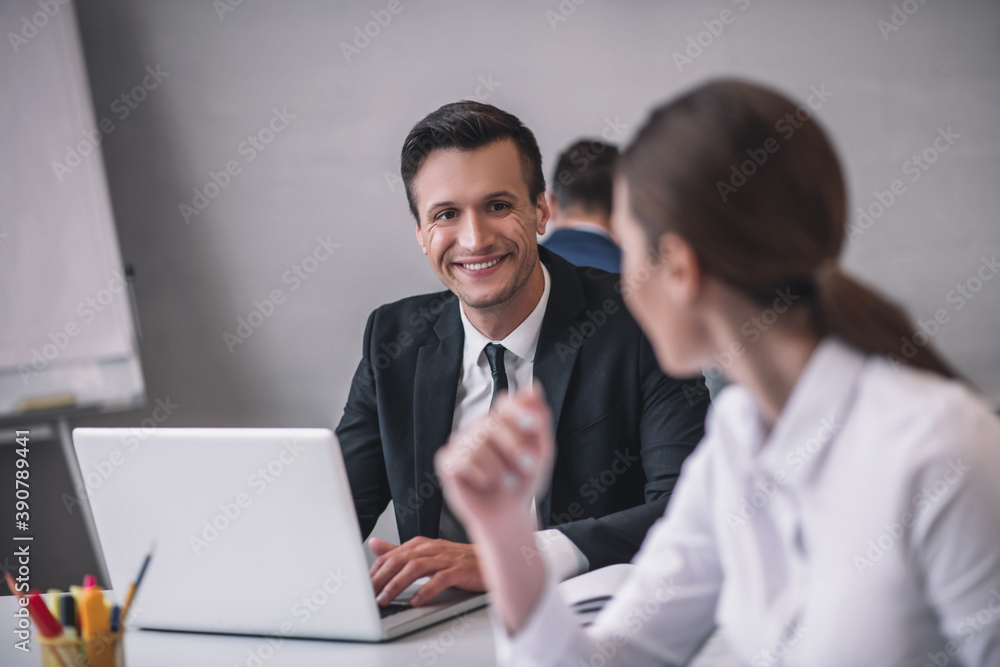 Smiling man behind laptop and woman sitting with back Smiling man behind laptop and woman sitting with back