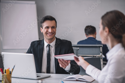 Man in tie taking folder from long-haired woman.