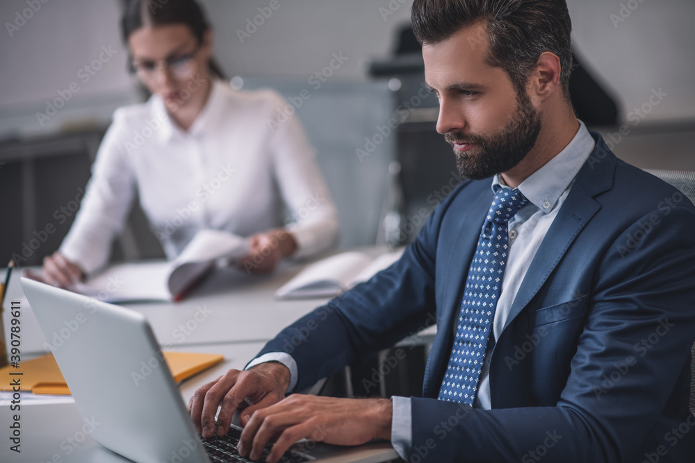 Business man working at laptop, woman sitting at distance Business man working at laptop, woman sitting at distance