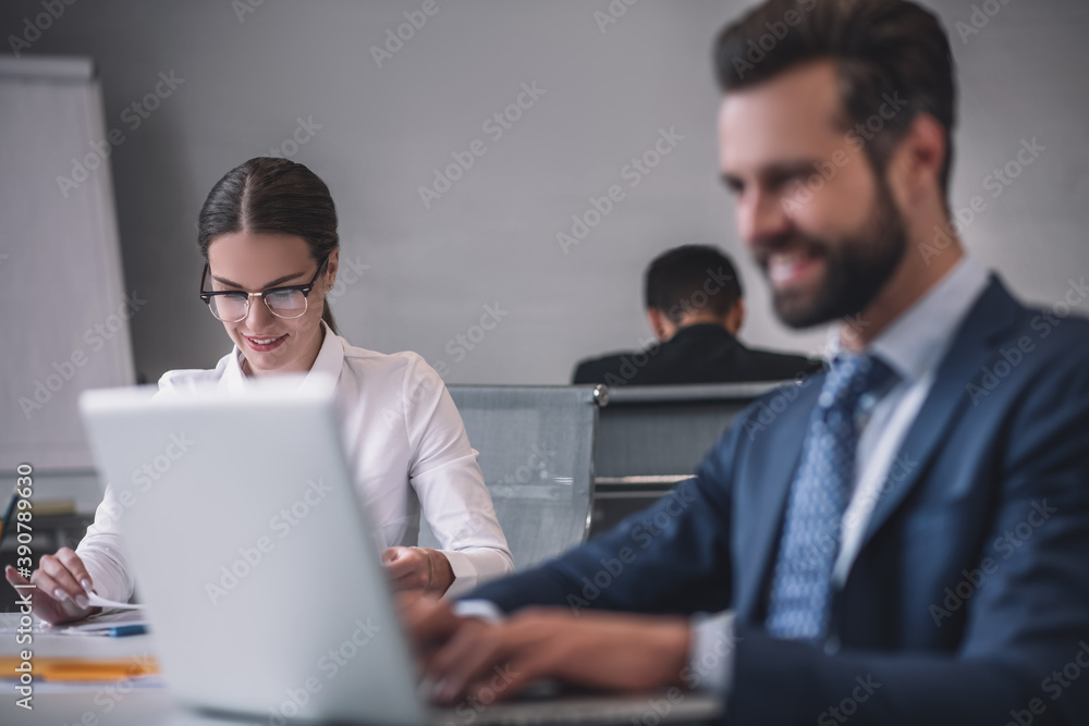 Smiling woman and man behind laptop in office Smiling woman and man behind laptop in office