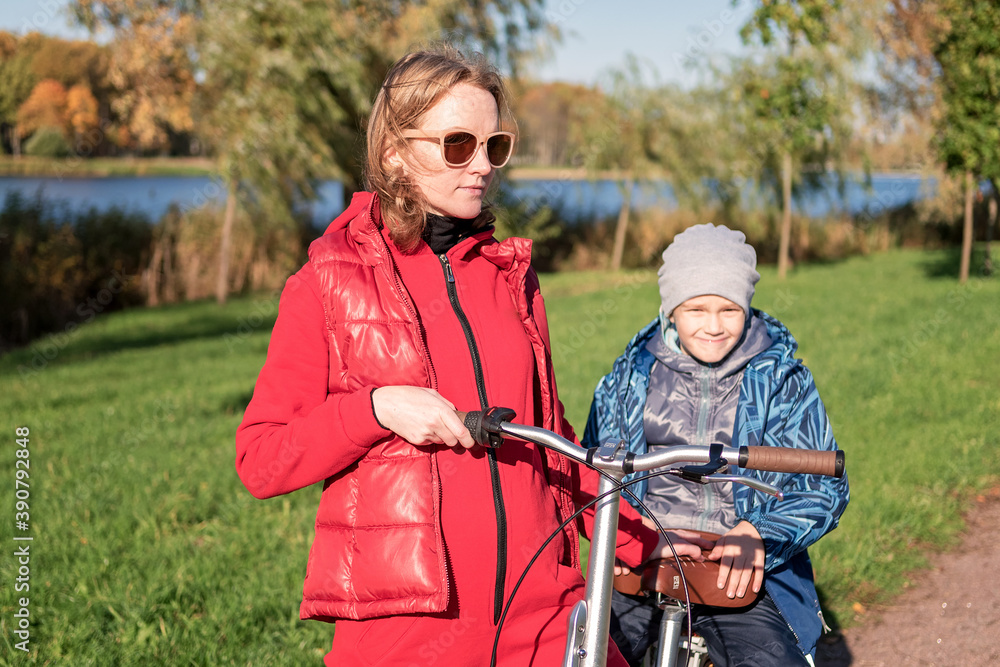 Mother in the autumn Park and teaching his son to ride a bike. The concept of raising a healthy person. Selective focus.