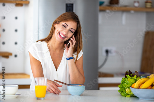 Beautiful young woman having breakfast in the kitchen. Shot of a young woman using a mobile phone while having breakfast in the kitchen at home
