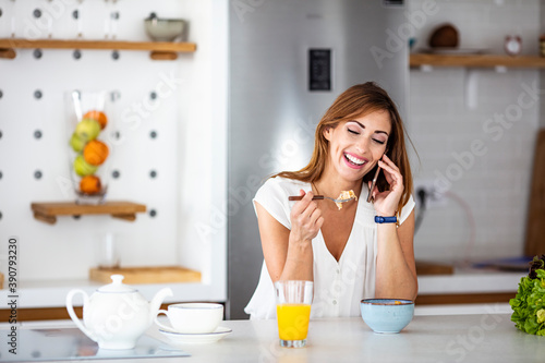 Shot of a beautiful young woman using a mobile phone in the morning at home. Shot of a happy young woman using her smartphone while relaxing in her kitchen at home