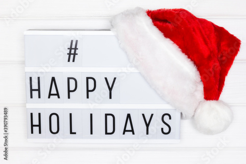 Happy holidays hashtag on white lightbox with red Santa hat