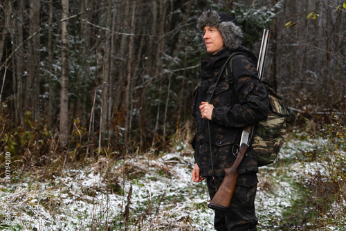 Hunter with a gun and a backpack in the winter forest 