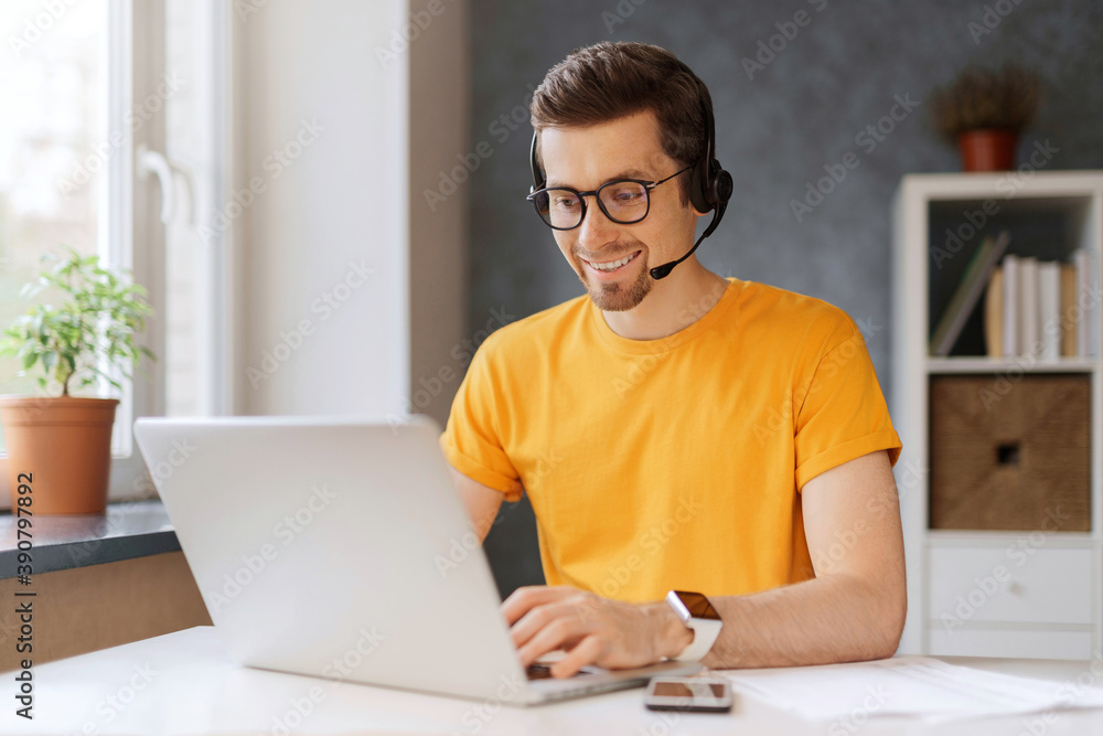 Happy programmer holding video call with colleagues clients partners. Сall center operator works from home. Man in glasses wearing headphones, enjoying watching educational online webinar on laptop