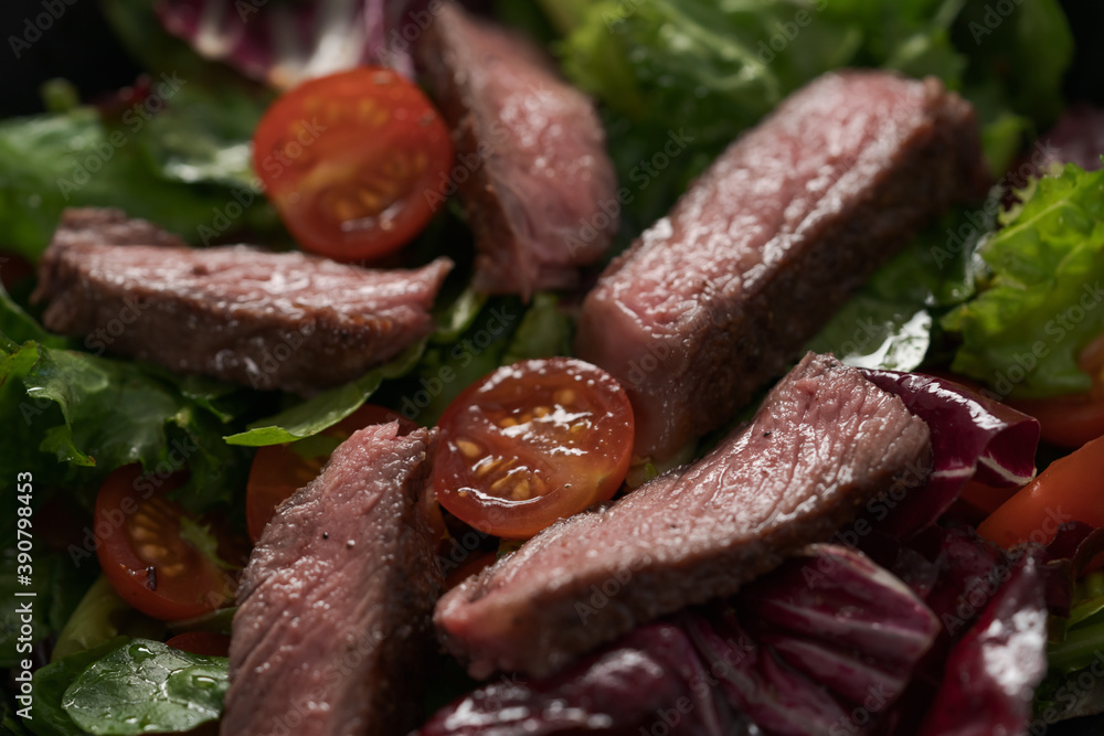 Steak salad with cherry tomatoes and mixed greens in black bowl