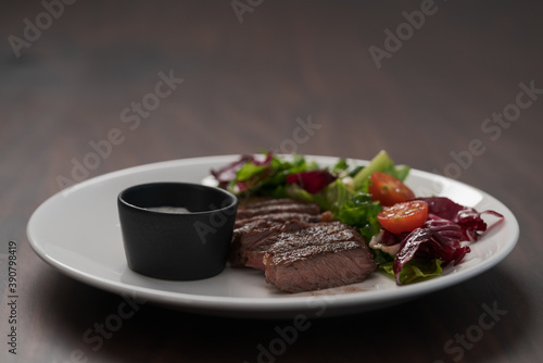 ribeye steak with garlic sauce and fresh salad on white plate on walnut table