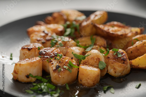 roasted scallops with baked potatoes wedges on a black plate