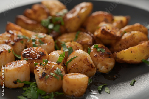 roasted scallops with baked potatoes wedges on a black plate