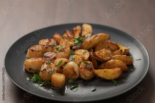 roasted scallops with baked potatoes wedges on a black plate on walnut wood background