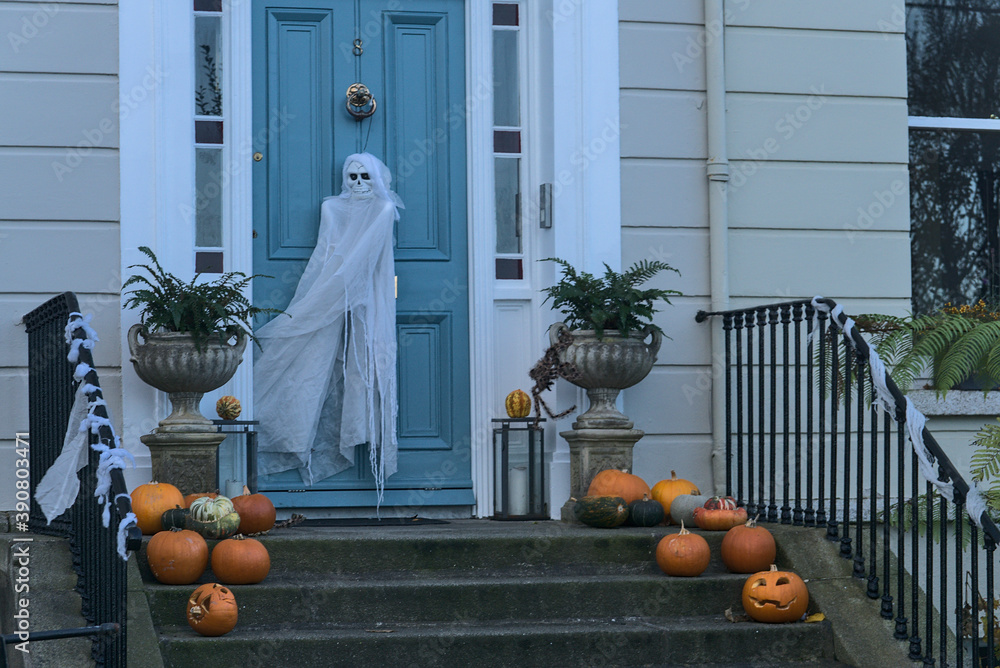 Fototapeta premium Spooky and beautiful Halloween decoration with many pumpkins, burning candle on the stairs and ghost on the door. Spooky and scary Halloween 2020 decoration, Dun Laoghaire, Dublin, Ireland