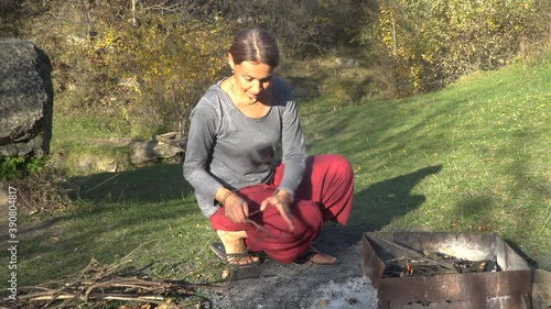 The woman breaking and putting dry twigs into the fire. Picnic in the mountains on a sunny autumn day