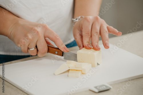 А close photo of the hands of a young woman who is cutting fresh butter on a cutting board with a sharp knife.