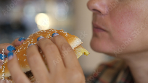 Young Hungry Woman Biting Vegan Meatless Burger in Fast Food Restaurant. Girl eating a hamburger. close-up shot. Fast food eats. Burger in female hands.