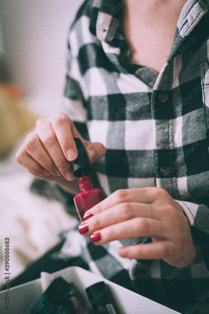 Obraz premium Woman with beautiful hands painting nails with red nail polish at home, side view. Close up shot.