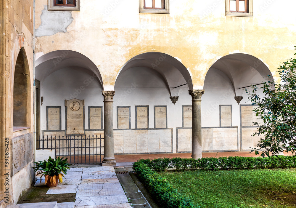 Courtyard of the Badia fiorentina, medieval church built in the 10th century, with vegetation, columns and tombstones, city center of Florence, Tuscany, Italy.