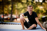 young smiling guy in black clothes sits on trampoline.