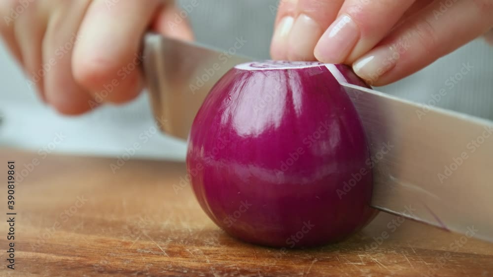 Slicing a red onion on a wooden cutting board in 4K. Concept of close-up look of a woman chef cutting onion.