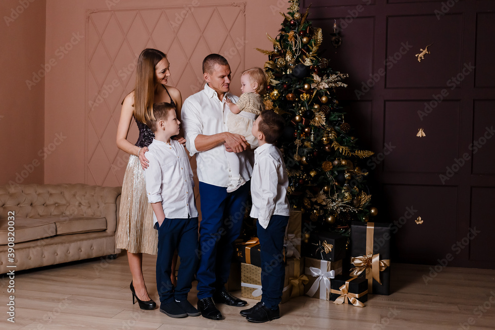 A family of five stands near a large Christmas tree. three children and parents