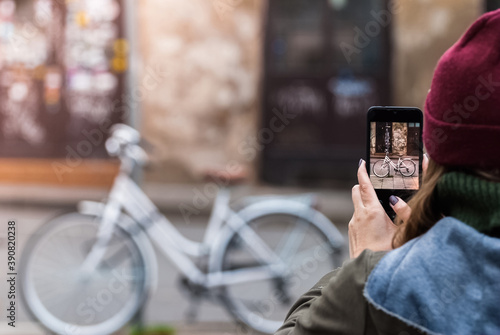 Woman taking photo of retro bicycle using the phone. Close-up shot of the hand holding the smartphone with the the urban facades behind.