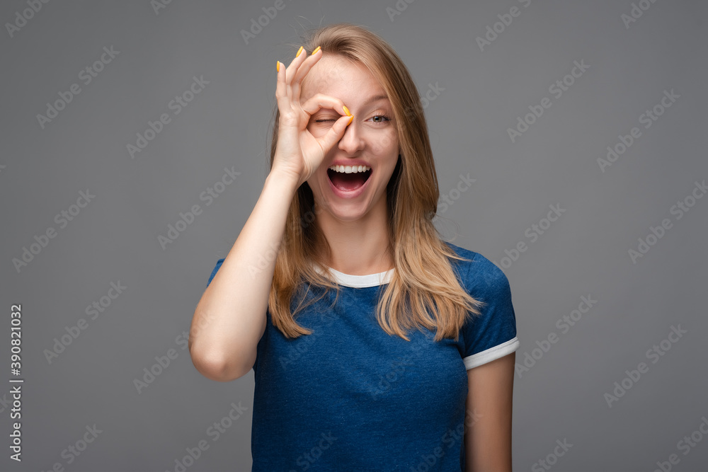 Cheerful smiling female looking at the camera through fingers in OKAY gesture. Face expressions, emotions concept. Cheerful smiling female looking at the camera through fingers in OKAY gesture. Face expressions, emotions concept.