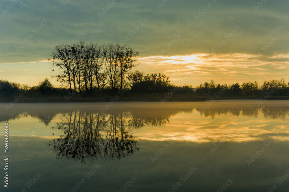 Reflection of evening clouds and trees in a misty lake