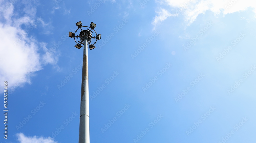 Spotlights on outdoor pillars. Public lamps with lifting systems in sports centers For illuminating at night On a blue sky background there are bright white clouds with a copy space. Selective focus Spotlights on outdoor pillars. Public lamps with lifting systems in sports centers For illuminating at night On a blue sky background there are bright white clouds with a copy space. Selective focus