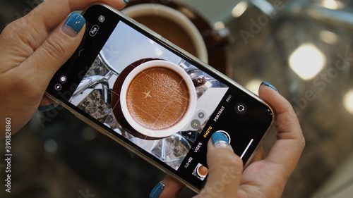 Close up of woman holds modern smartphone and taking pictures of cocoa to share photos on social media resources