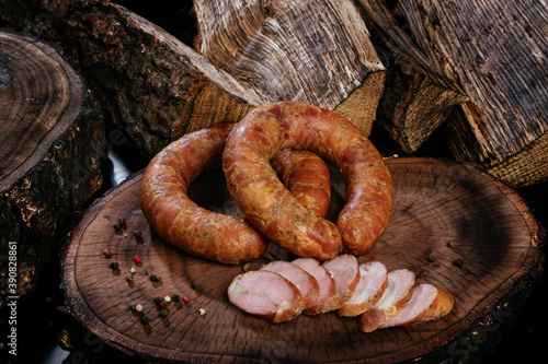 Two rings of smoked sausage on top of each other, pegs of sausage slices, on a wooden stump dark background.
