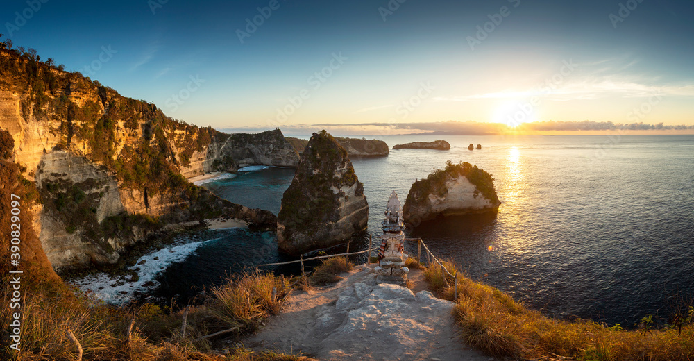Fototapeta premium Panorama sunrise over steep cliffs and crystal clear ocean with small temple in foreground at Thousand Islands viewpoint, Nusa Penida, Bali, Indonesia