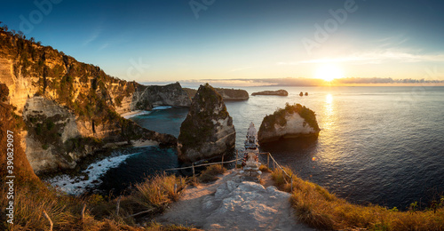 Panorama sunrise over steep cliffs and crystal clear ocean with small temple in foreground at Thousand Islands viewpoint, Nusa Penida, Bali, Indonesia