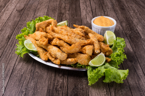Portion of breaded fried fish served on lettuce leaves with lemons and tartar sauce to accompany the food. Gastronomic photography of fish.