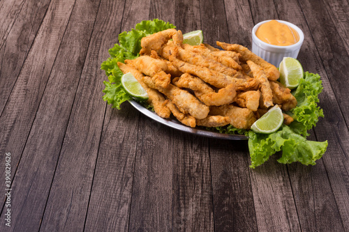 Portion of breaded fried fish served on lettuce leaves with lemons and tartar sauce to accompany the food. Gastronomic photography with left space for texts.
