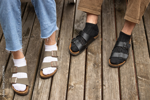 Guy in black socks and girl in white socks on the old wooden floor. both in sandals. close-up.