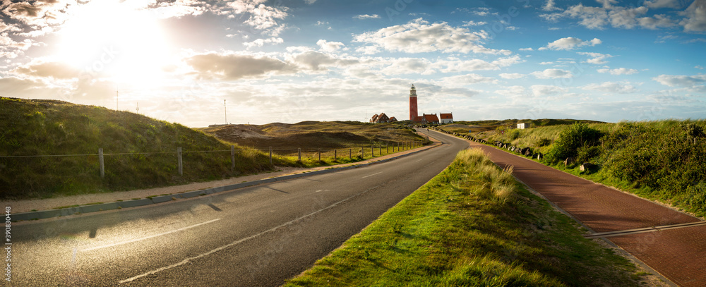 Road to iconic lighthouse surrounded by houses during sunset at the island of Texel, The Netherlands - obrazy, fototapety, plakaty 