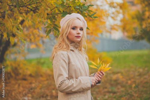 Beautiful young woman with fall yellow leaves walking in park