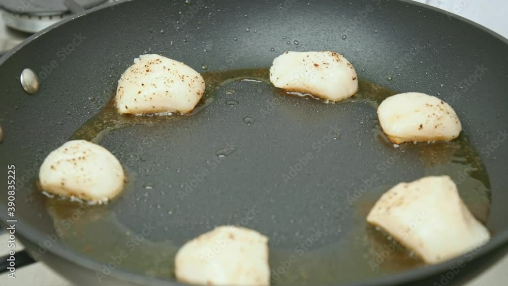 Close-up frying Raw Sea Scallops into a pan with oil on a gas stove in 4K. Concept of cooking scallops with salt and pepper, flipping around, and checking for a well-done cook in slow-motion.