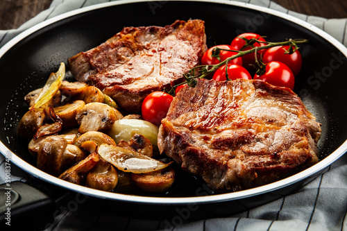 Pork steaks in frying pan with champignons, onion and tomatoes