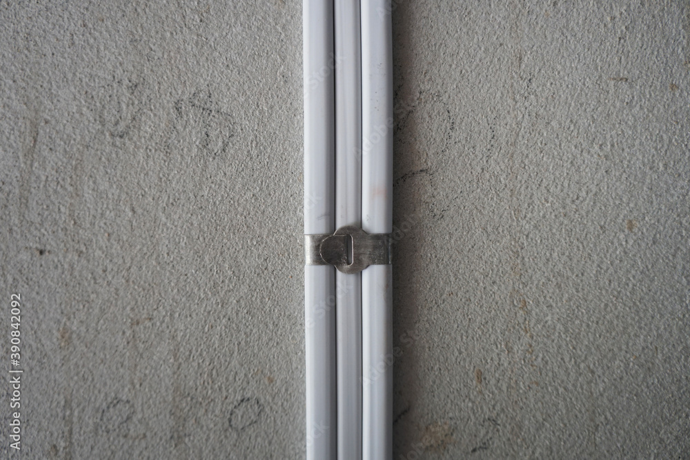 White electric cable attach on the cement wall with aluminum cable clip. PVC insulated electrical wiring. With strap belt. White electric cable attach on the cement wall with aluminum cable clip. PVC insulated electrical wiring. With strap belt.