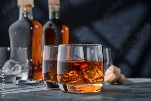 Two round glasses of whiskey with ice on a concrete table, on a blue background.