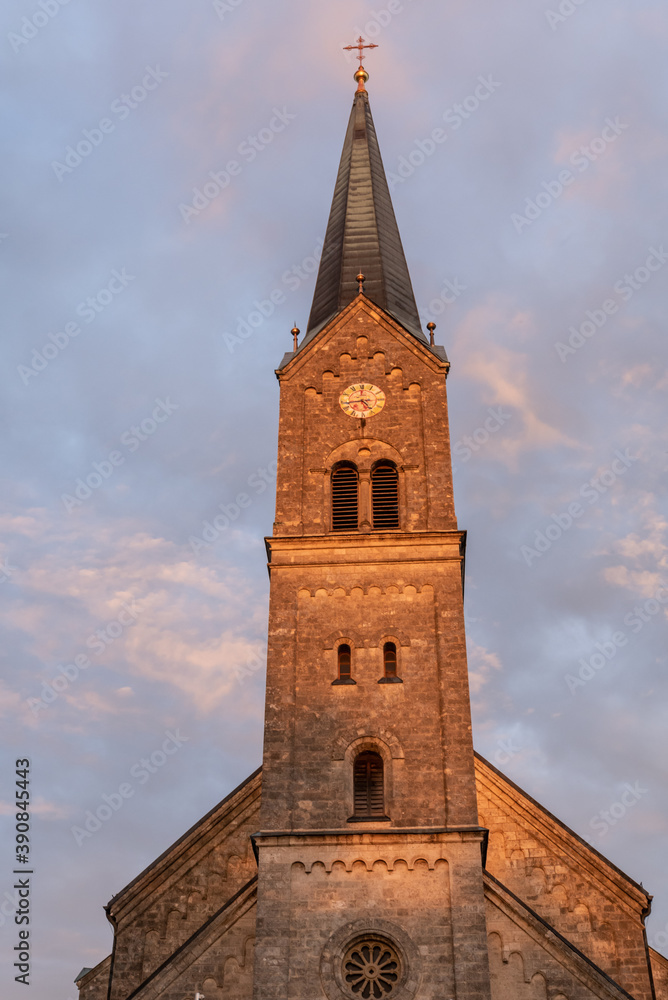 Kirchturm im Abendlicht vor Wolke und blauem Himmel