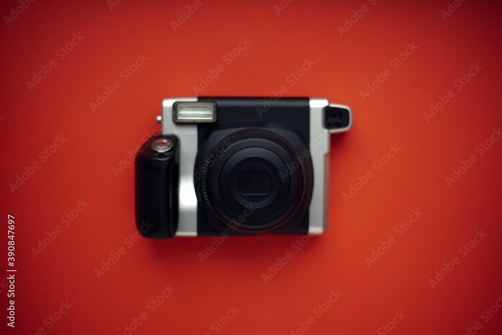 A modern black instant print camera on a bright red background.